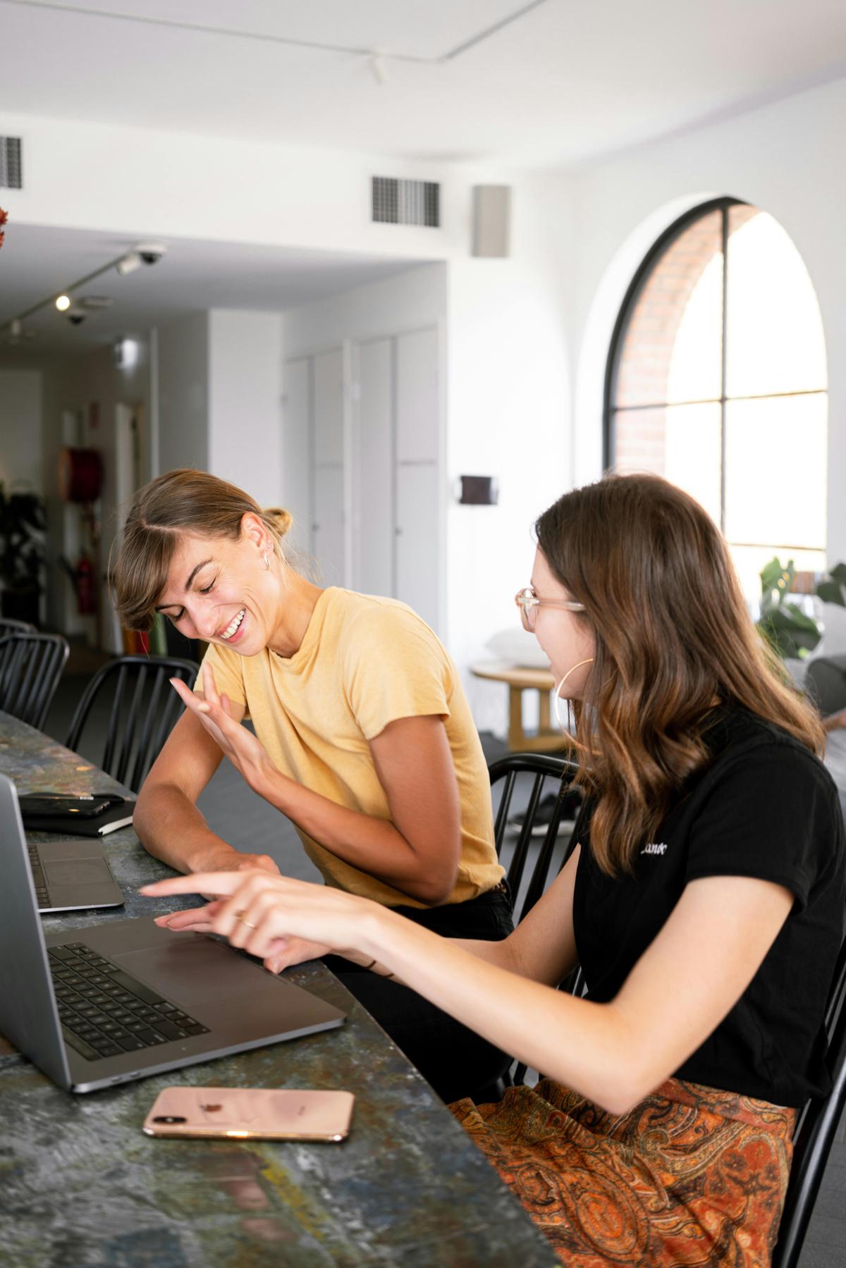 Two professional women collaborating at a laptop in a modern workspace